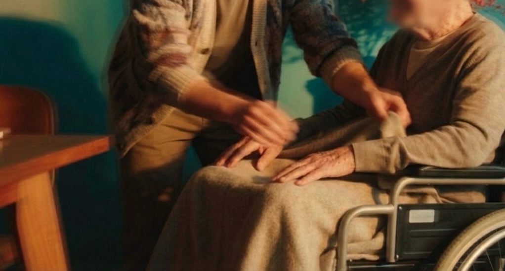 Hands of a caregiver gently resting on the lap of an elderly person in a wheelchair